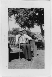Elderly African American man seated in a chair with a cane. 
