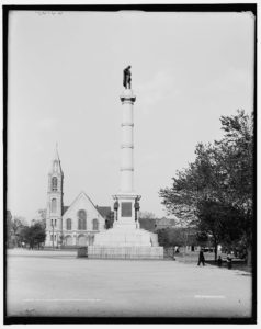 Statue on a marble column with buildings in background.