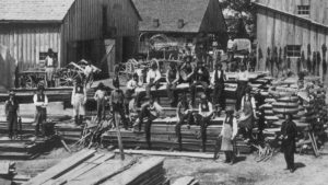 Group of Black men sitting on lumber and standing in pose for a group photograph. 