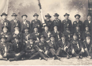 Elder men in suits posed in a group shot with a Black man holding a flag. 