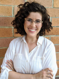 Portrait of a woman in a white shirt with a brick background. 